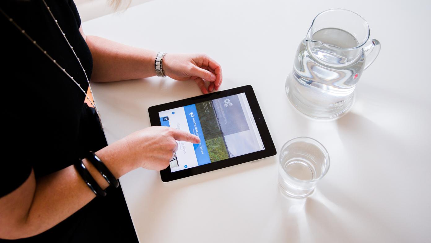 Person swiping on their iPad with a glass of water.