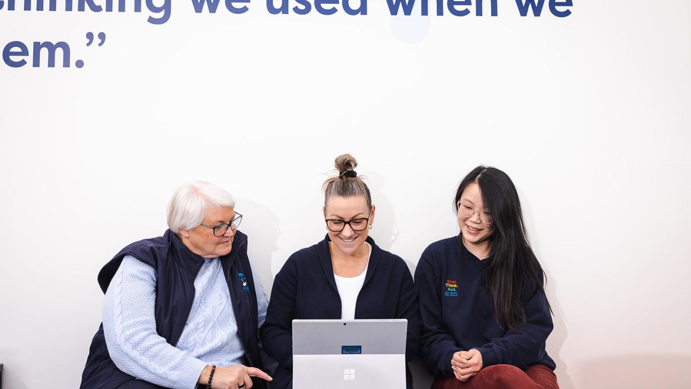 Bev, Nat and Shin working collaboratively on a screen and smiling.