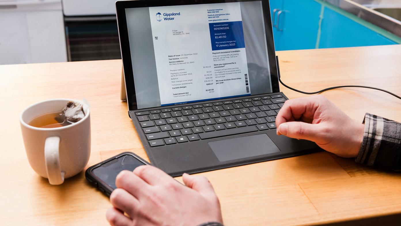 A customer sitting at the kitchen bench looking at their bill on a laptop. 