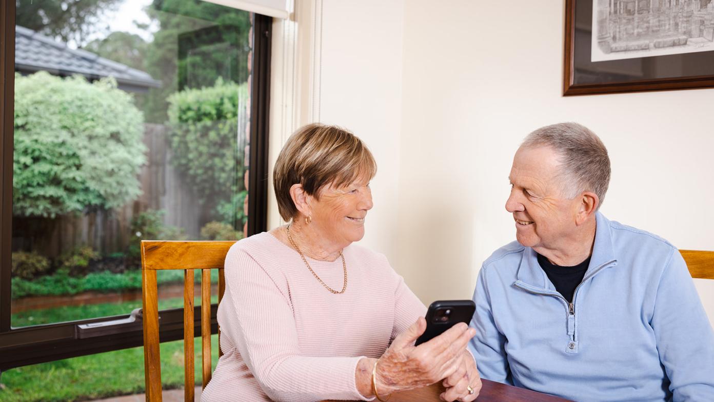 Man and woman smile at each other while holding phone.