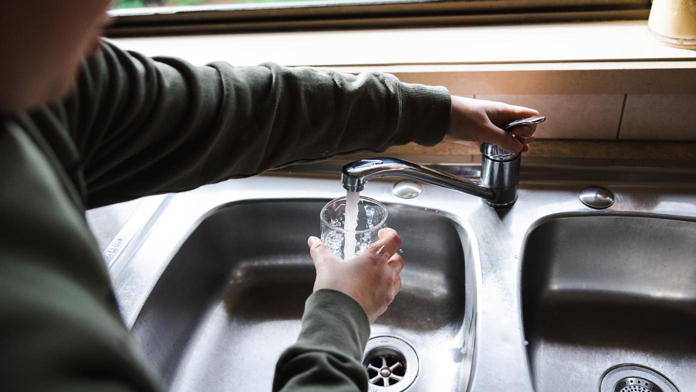Person fills up a glass of water at the sink. 