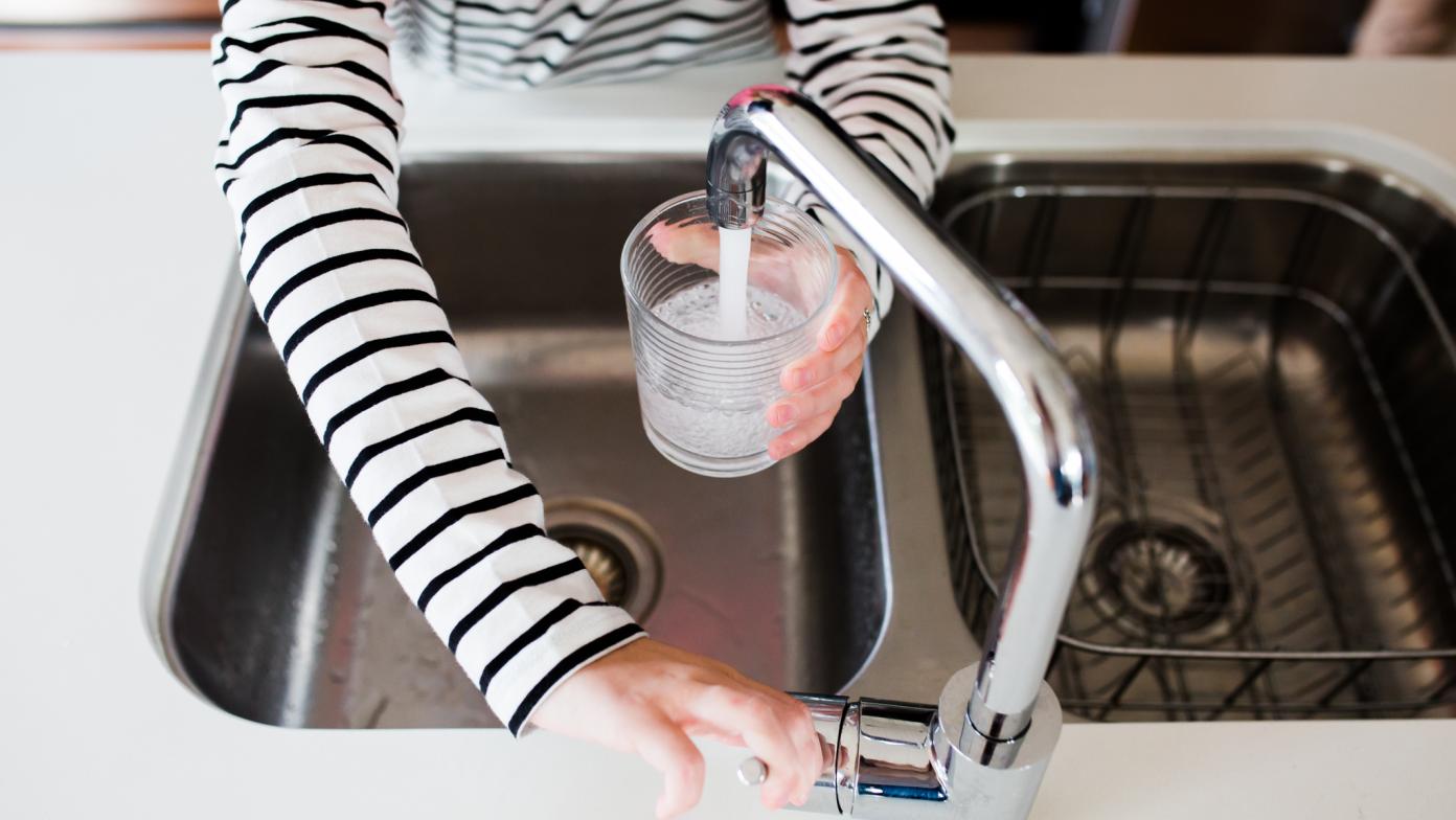 Kid filling up a glass of water from the tap.