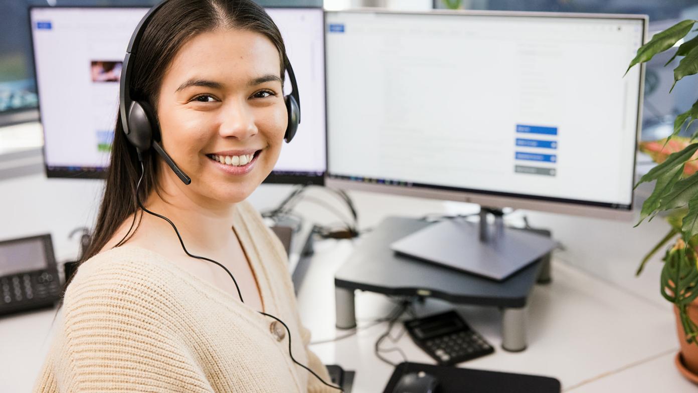 Woman at computer with headset on, she is smiling