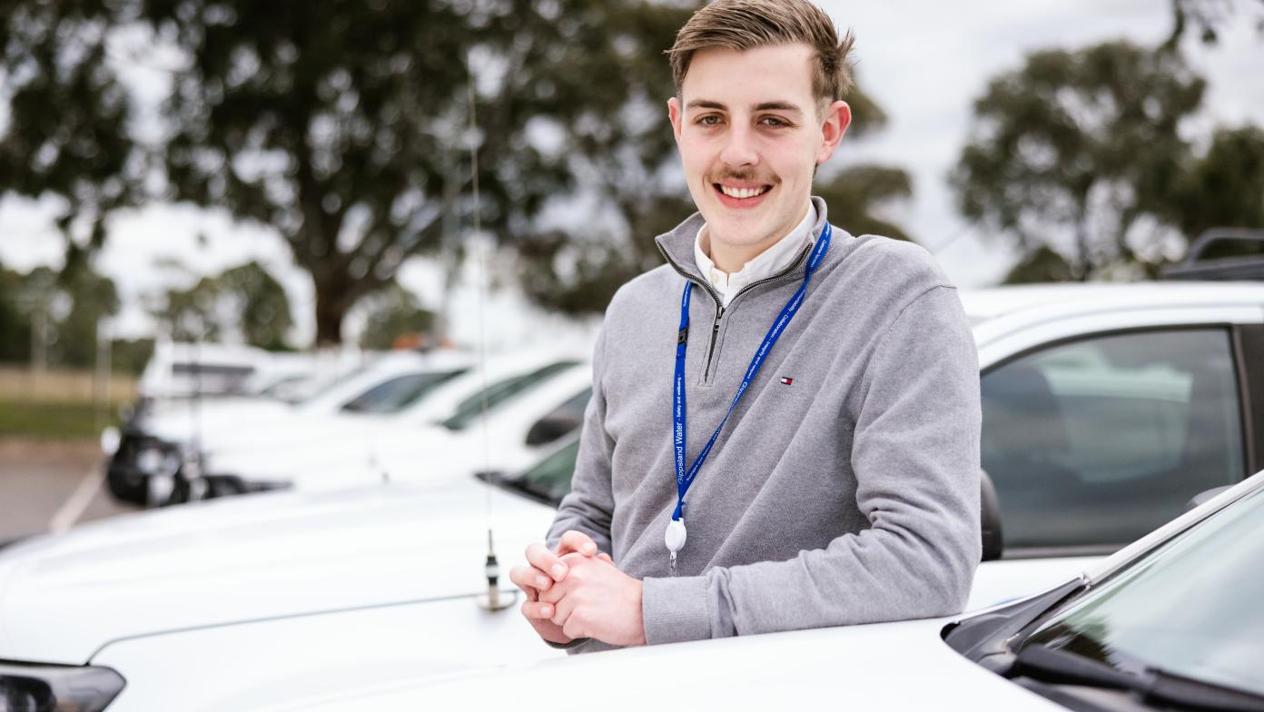 Young man standing near Gippsland Water vehicles.