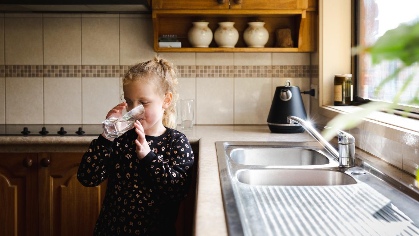 Young girl drinking a glass of water in a kitchen.