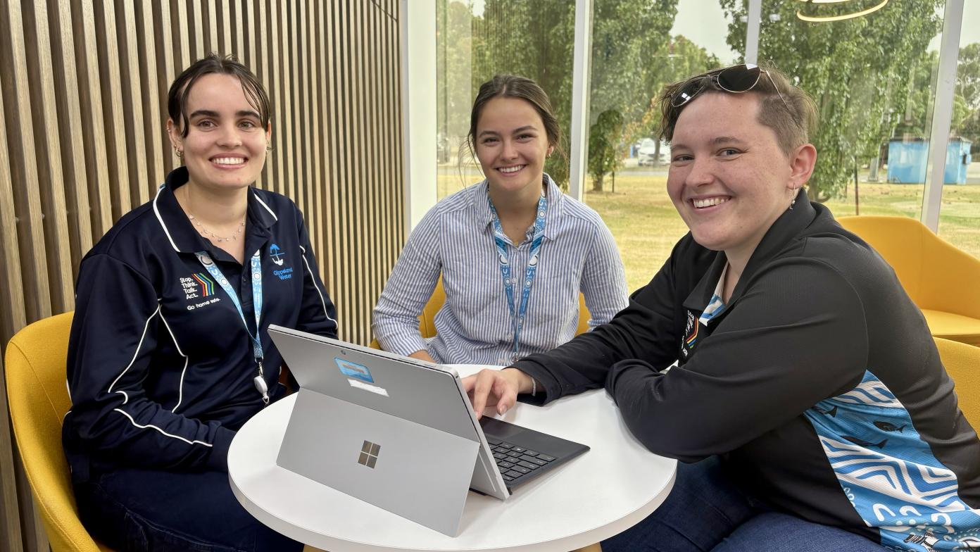Three women sit at a table and smile at the camera.