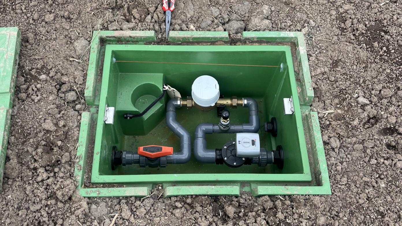 Green box in ground with small pipes and devices.