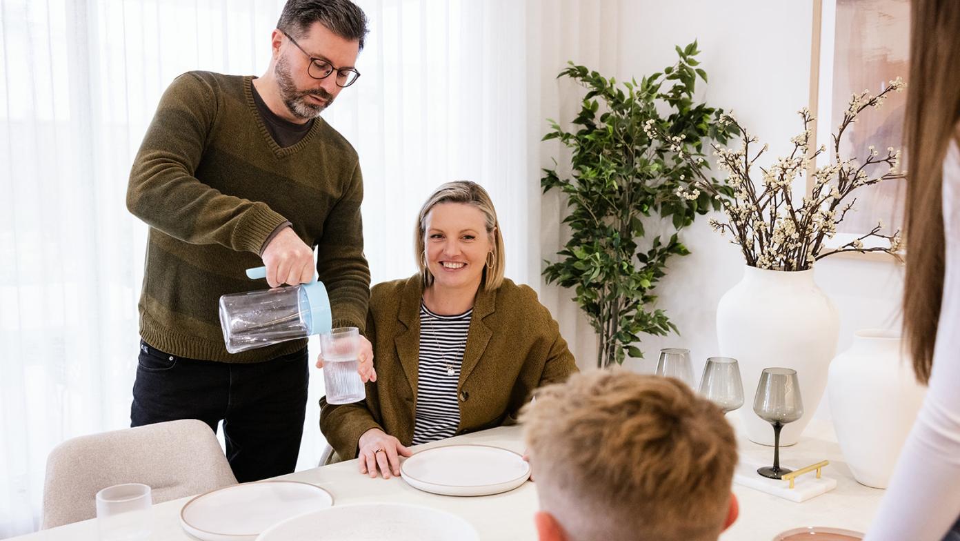 Dad pours water into a glass at table surrounded by family