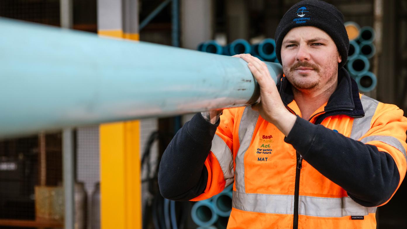 Gippsland Water employee carrying a length of pipe. 
