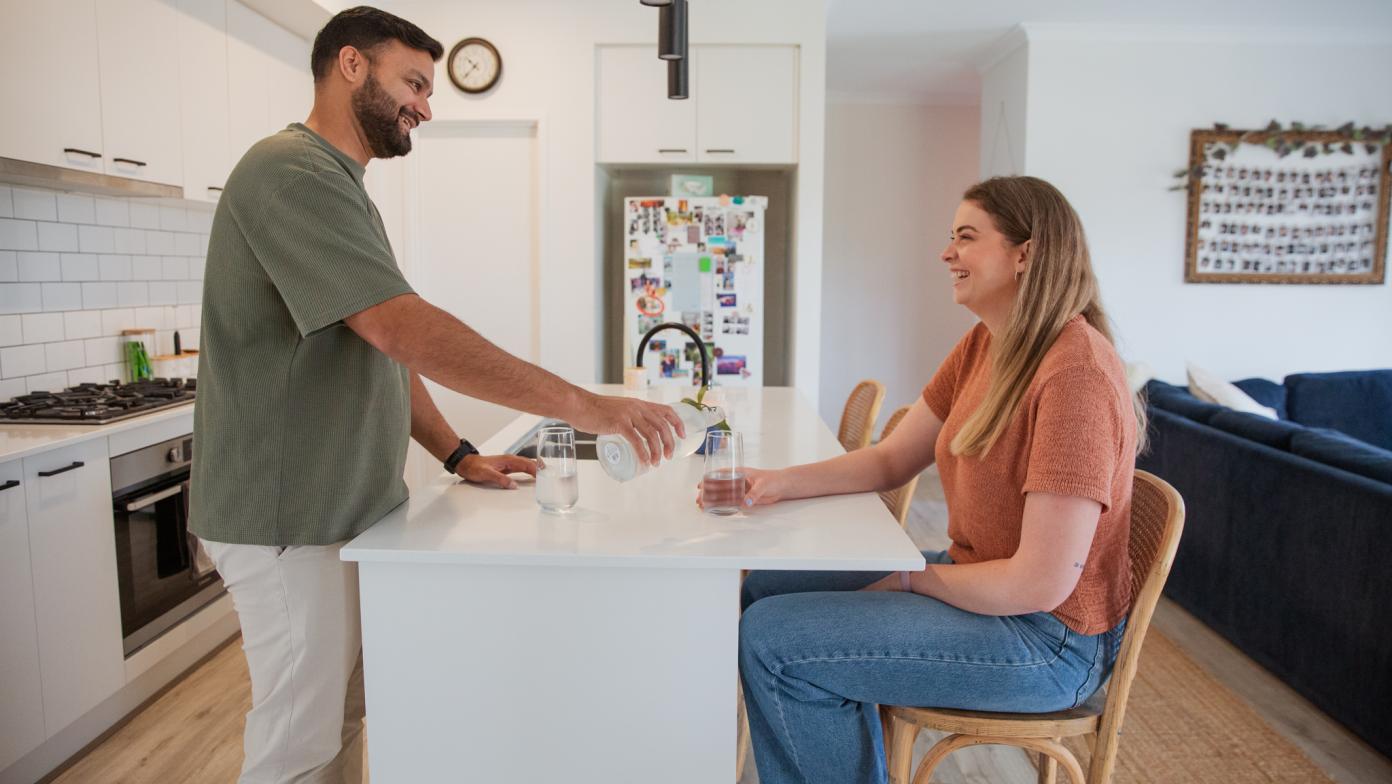 A man and a woman in a kitchen pouring a glass of tap water.