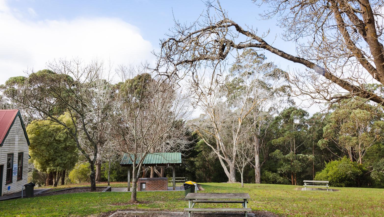 Moondarra Reservoir picnic area. A picnic table is in the foreground, and a public barbeque space and Cecil in are pictured in the background.