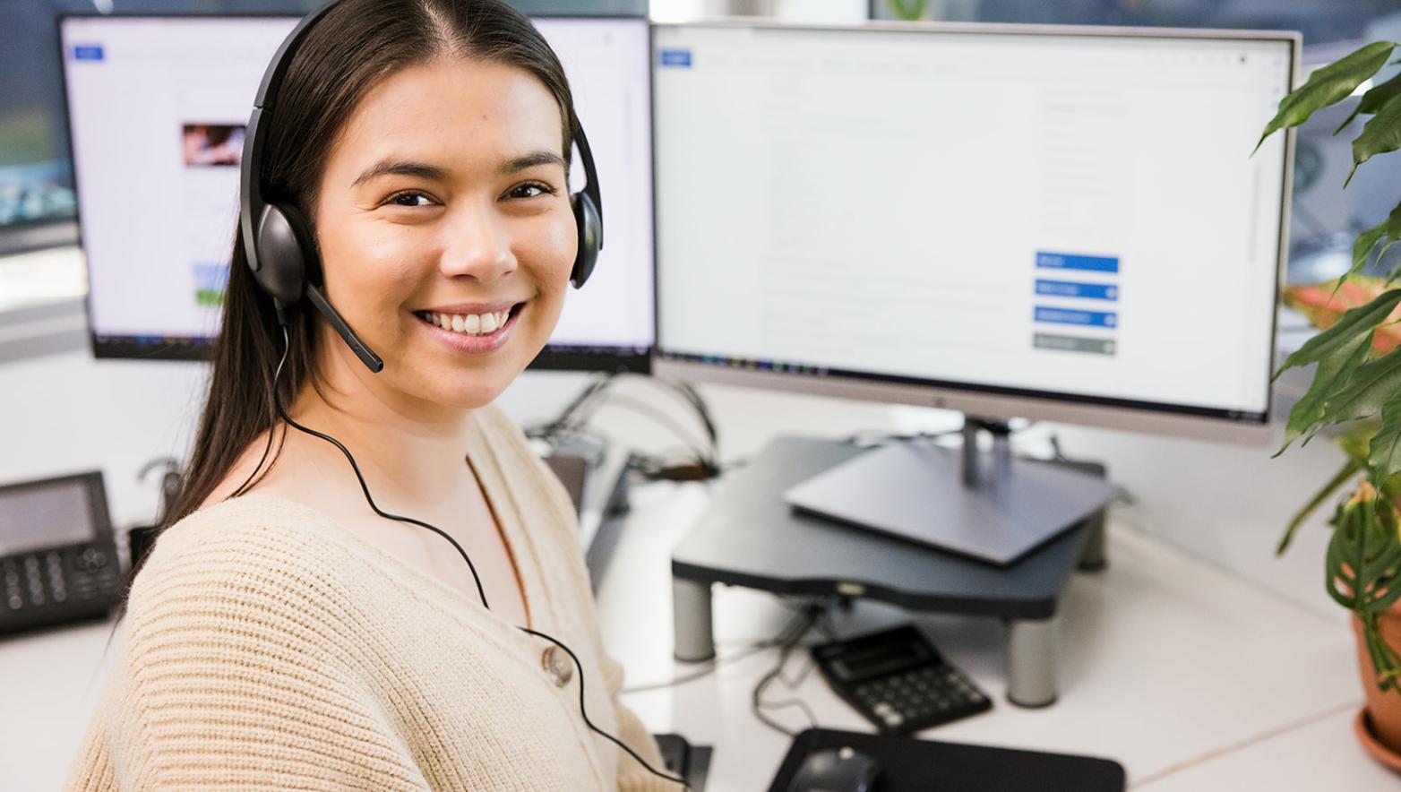 Woman at computer with headset on, she is smiling