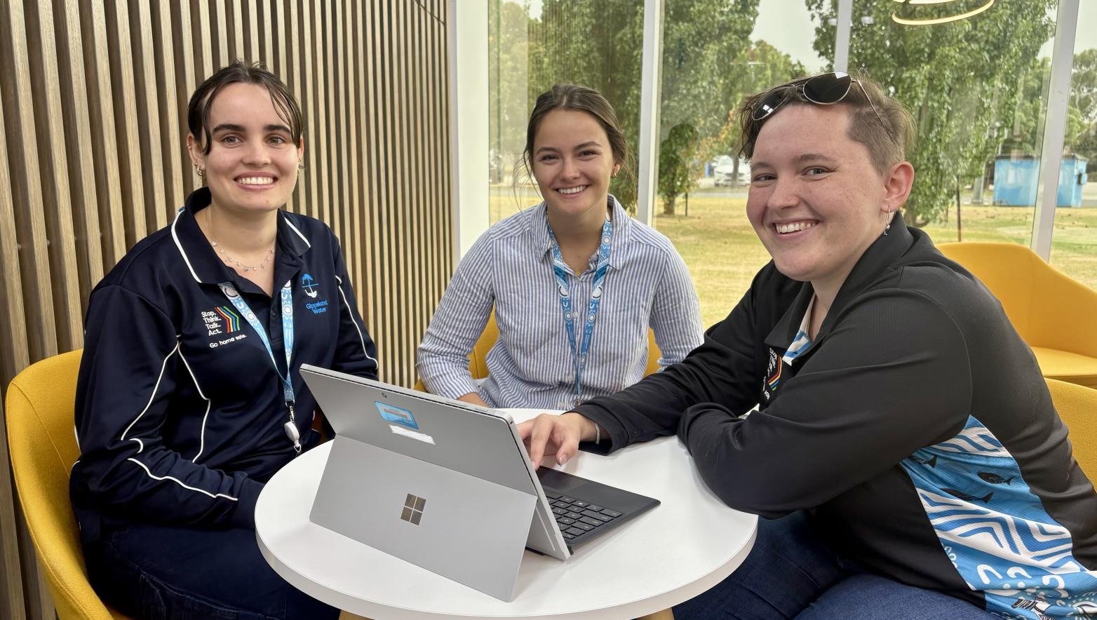 Three women sit at a table and smile at the camera.