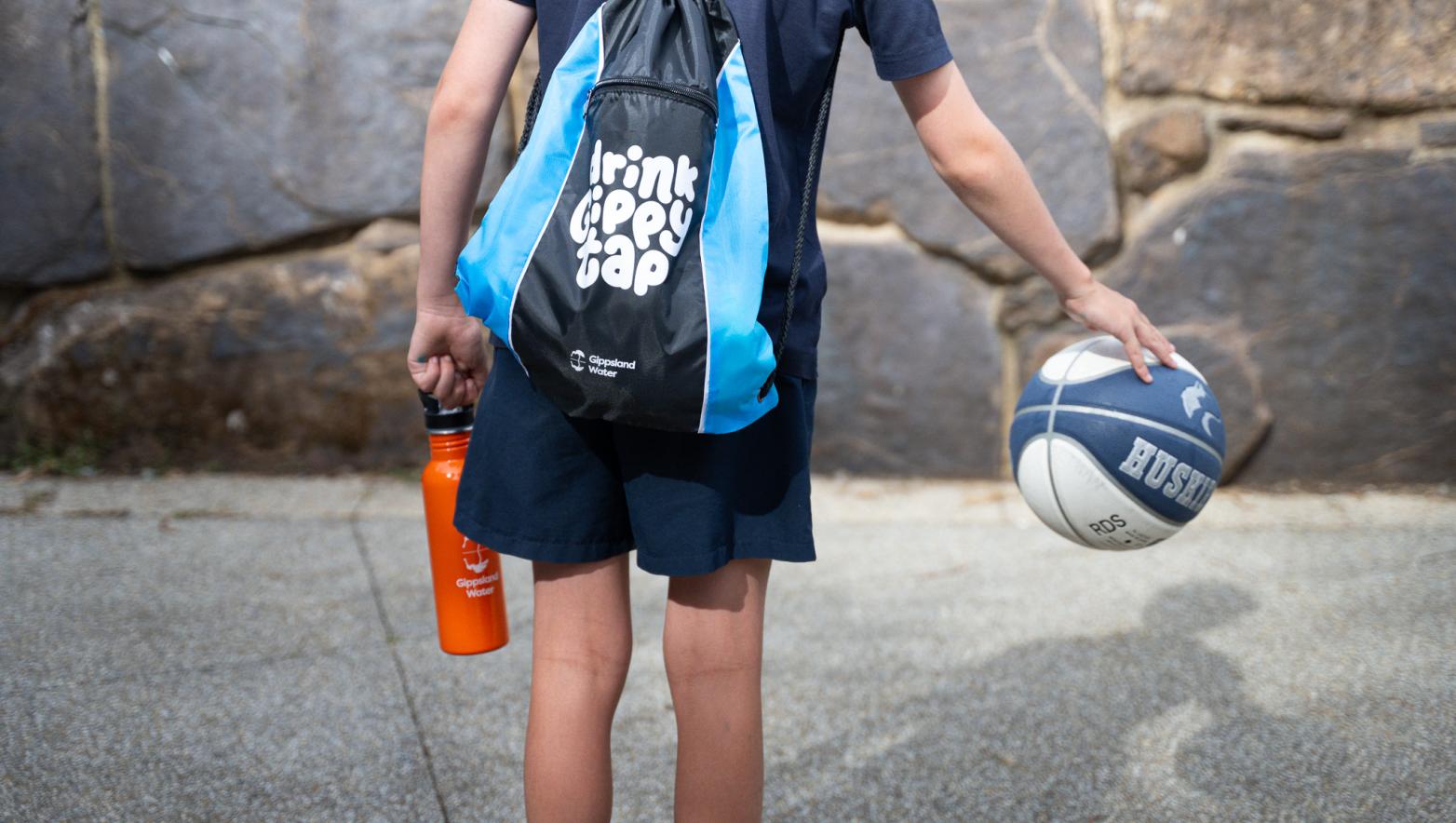 Boy with bag and basketball faces away from camera