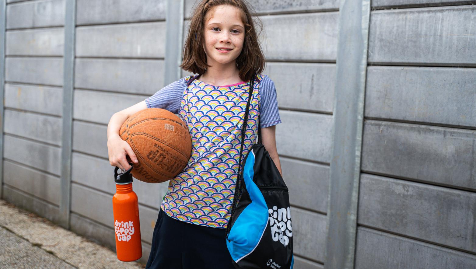 Girl holding drink bottle, bag and basketball