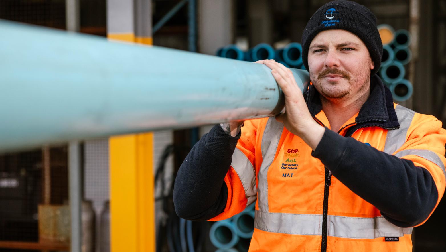 Gippsland Water employee carrying a length of pipe.