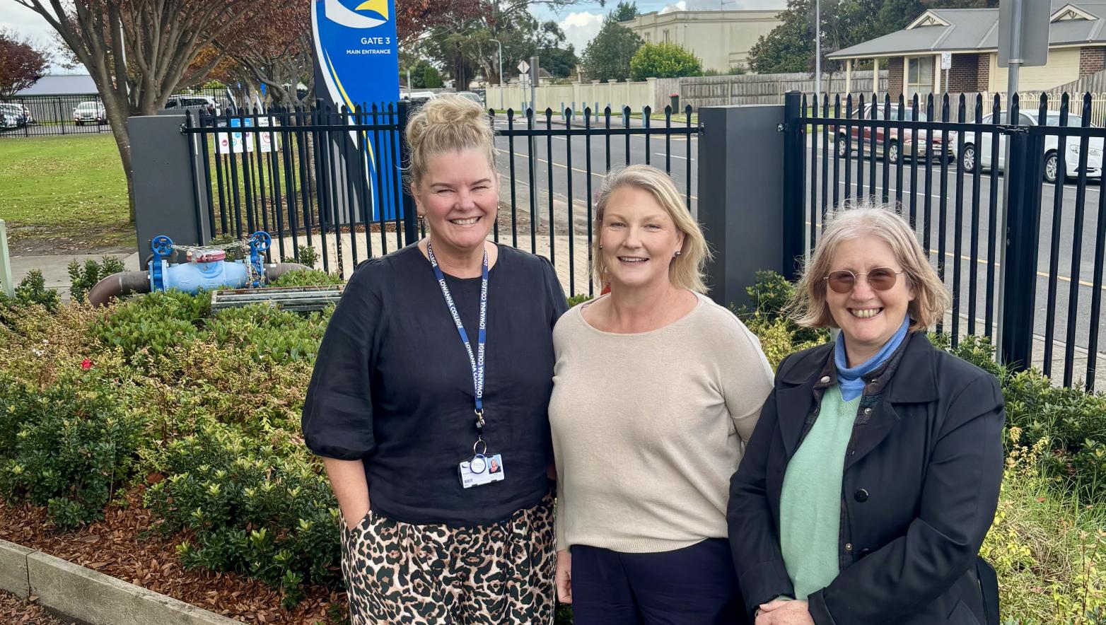 Three people standing next to a school fence
