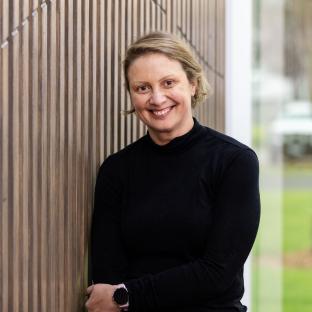 A blonde woman smiling looking at the camera leaning against a textured wall