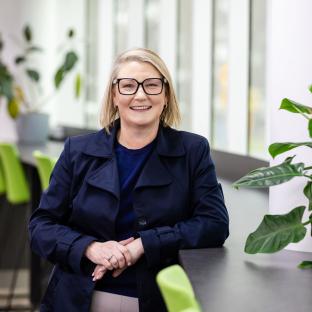 A woman leans against the table smiling at the camera