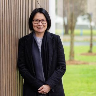 A woman looking at the camera smiling and leaning against a textured wall