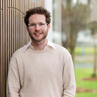 A man looking at the camera smiling standing against a textured wall